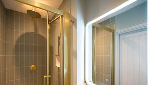 Un baño moderno con cabina de ducha de vidrio, perchero visible y puerta con iluminación.