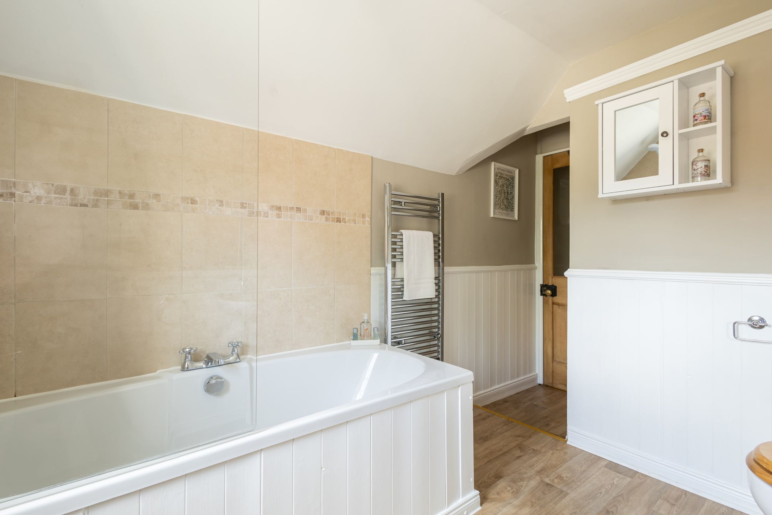 A bathroom with a large bathtub, a towel rack, a toilet, and a mirror cabinet.