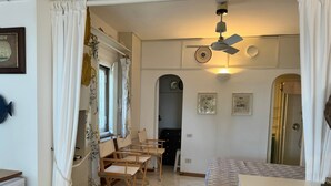 Egy hangulatos szoba, amelyben található egy ágy, egy íróasztal és egy szék. Van benne egy ablak, amelyen függöny van, egy mennyezeti ventilátor és egy ajtó, amely egy másik szobába nyílik.