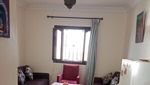 Un espacio habitable pequeño con piso a cuadros, un sofá, una silla, una mesita y un refrigerador.