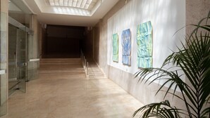 Een gang met een glazen deur aan de linkerkant, een trap en een muur met abstracte kunst.