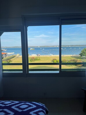 Enjoy a serene coastal view from the large window, featuring a grassy area and boats on the water.