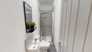 Ein schmales Badezimmer mit Toilette, Waschbecken und einer Duschkabine.