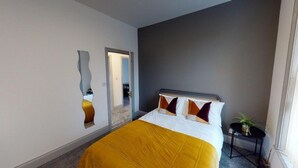 Ein Hotelzimmer mit Bett, Spiegel, kleinem Tisch mit Pflanze und einer Tür zu einem anderen Raum.