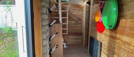 Un interior moderno con una escalera de madera, una zona de cocina con ollas colgantes y vistas a través de una puerta de cristal.