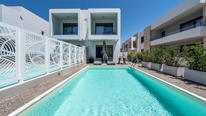 Un espace piscine moderne avec une piscine à l’eau d’un bleu limpide, des bâtiments blancs et une clôture décorative blanche.