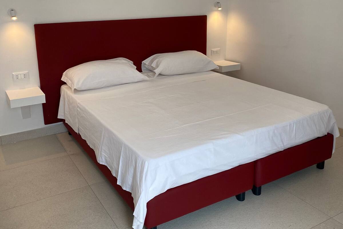 Un dormitorio moderno con cabecera roja, ropa de cama blanca y lámparas de noche.