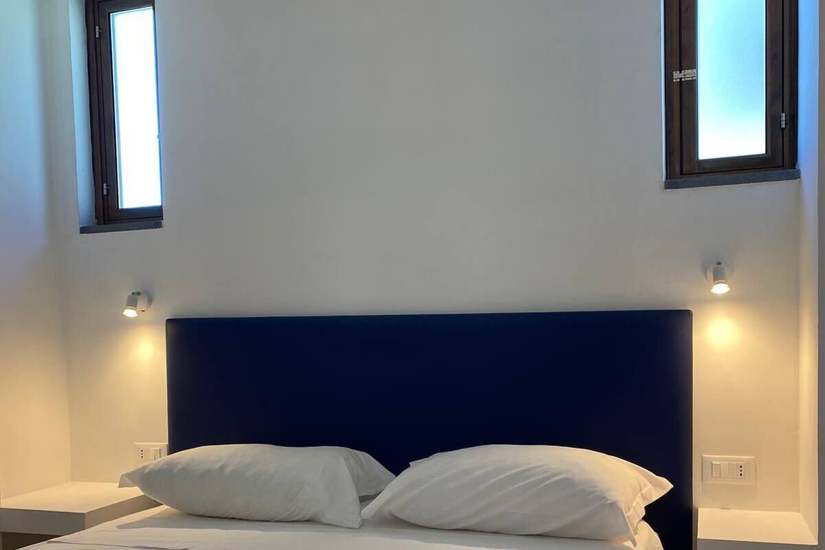 Un dormitorio con una cama grande, dos mesitas de noche y dos luces fijadas a la pared.