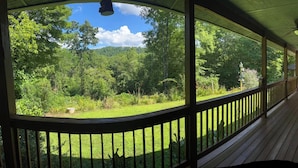 Eine überdachte Veranda mit Blick auf eine üppige, grüne Landschaft und eine Holzterrasse.