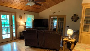 Ein Wohnzimmer mit braunem Ledersofa, Fernseher, Holzboden und Deckenventilator.