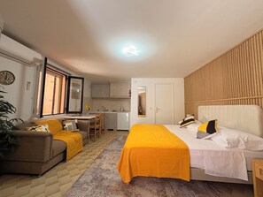 Ein Hotelzimmer mit Bett, einer Couch, einem kleinen Tisch, einem Sessel, einer Küchenzeile und einer Tür.