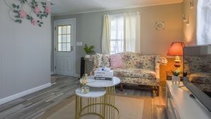Un salón con un sofá floral, una mesa de centro redonda con libros, una lámpara y un televisor.