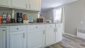 Una cocina con armarios blancos, una estación de café y un ventanal con cortinas.