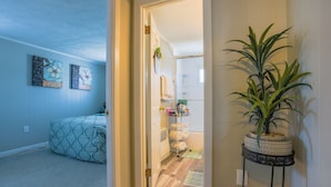 Un pasillo con una cama, una planta y una puerta que da a un baño.