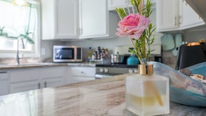 Una cocina con armarios blancos, encimera de mármol y un florero con una flor rosa.
