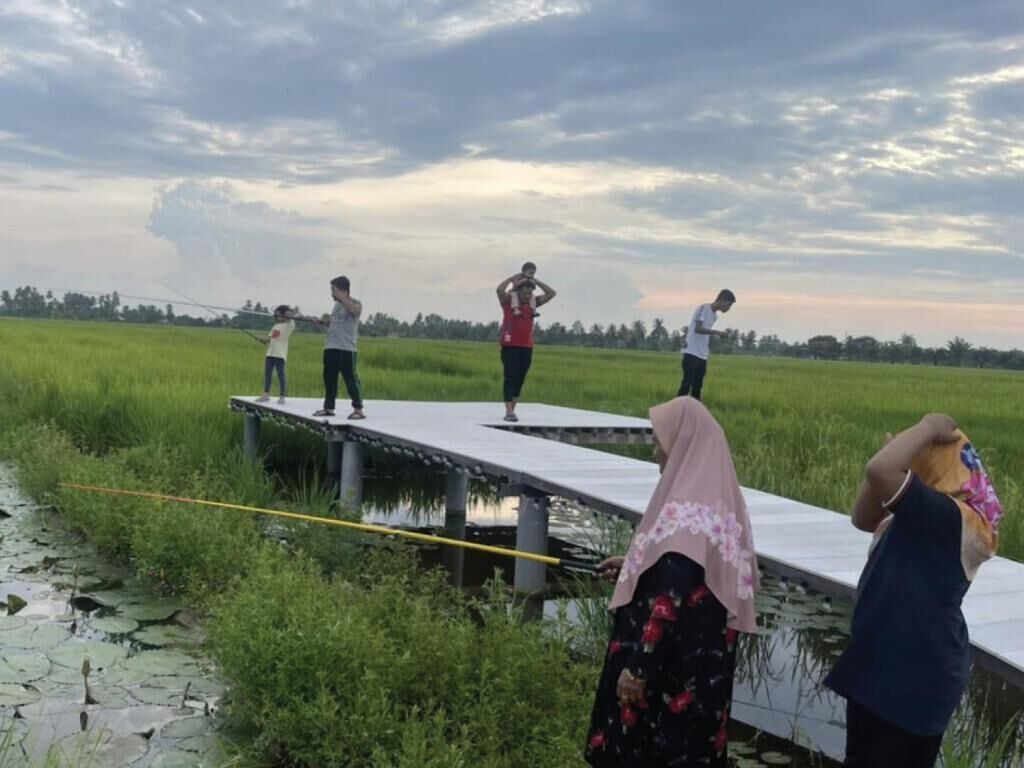A group of people on a wooden bridge over a body of water, surrounded by greenery.
