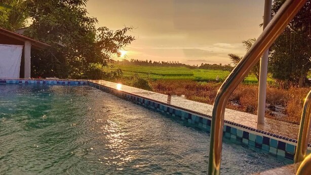 A swimming pool with a tiled edge, surrounded by greenery and a sunset in the background. - Kurau Inn  Farmstay (Kuala Kurau)