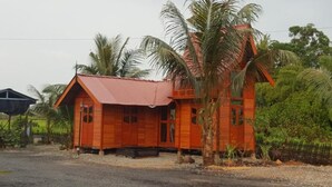 A small, single-story wooden house with a red roof, surrounded by palm trees and greenery. - Kurau Inn  Farmstay (Kuala Kurau)