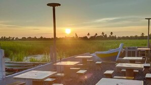 A sunset view with a row of tables and chairs, a boat, and a water body. - Kurau Inn  Farmstay (Kuala Kurau)