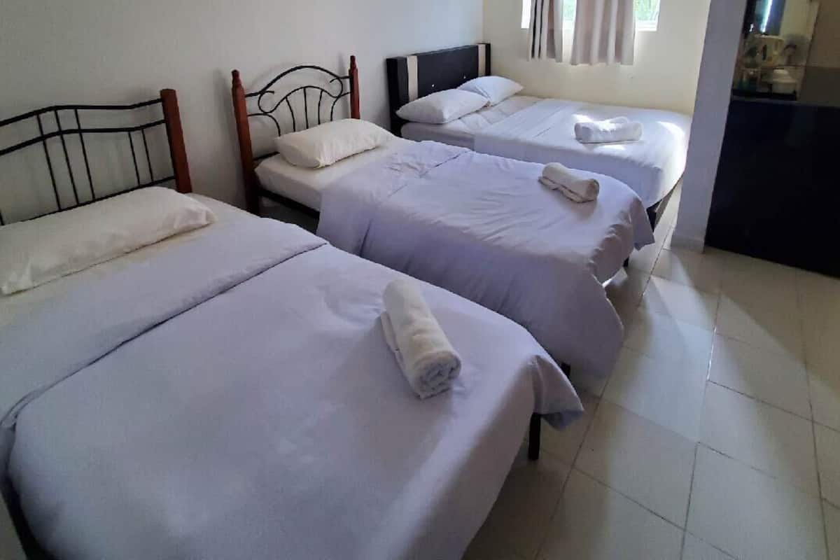 Una habitación con tres camas individuales, cada una con cabecero de madera y ropa de cama blanca.