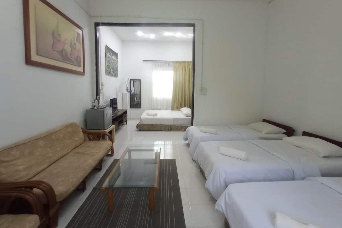 Habitación de hotel con sofá, una mesa de vidrio, dos camas individuales, un televisor y un escritorio con computadora.