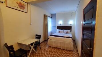 A hotel room with a bed, a desk, a chair, and a door.