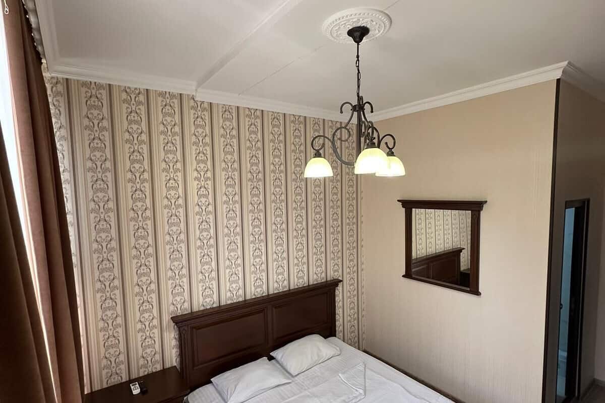 A hotel room with a large bed, a nightstand, a dresser, a mirror, and a chandelier.