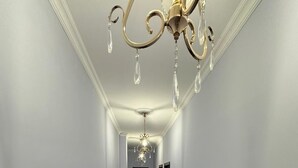 A hallway with a chandelier, a wooden bench, and a door at the end. - AİSİ HOTEL (Kutaisi)