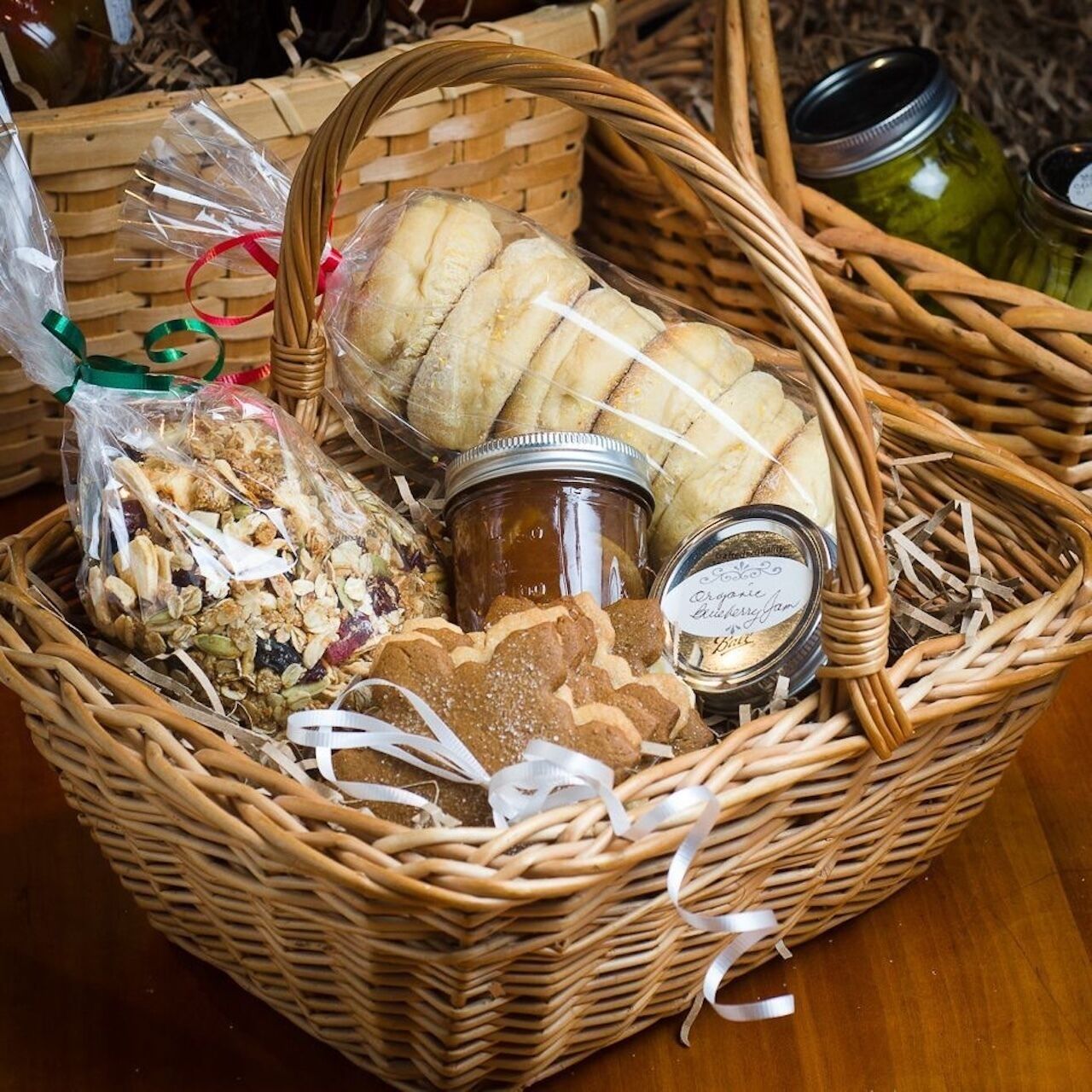 A wicker basket filled with various food items including cookies, granola, and jars of preserves.