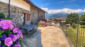 A stone building with a patio, outdoor seating, and a view of mountains. - La Volta - Molino Maufet (Colico)