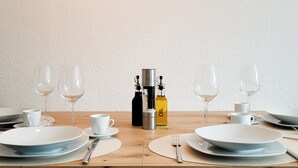 Een eettafel gedekt met borden, bestek en glazen, met een koffieapparaat en een fles olie in het midden.