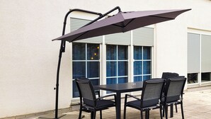 Een terras buiten met een tafel en stoelen, een grote parasol en een raam met luiken.