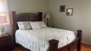 Ein Schlafzimmer mit einem hölzernen Bett, einem Nachttisch, einer Lampe und zwei gerahmten Bildern an der Wand.