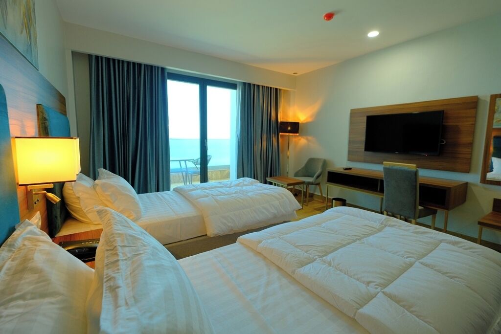 A hotel room with two beds, a TV mounted on the wall, a desk, and a chair.