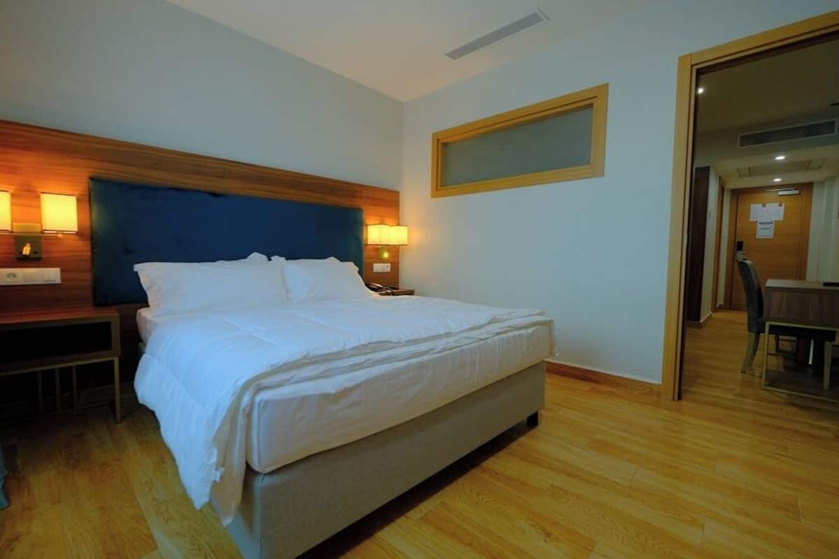 Habitación de hotel con una cama grande, cabecera de madera, dos lámparas de noche y suelo de madera.