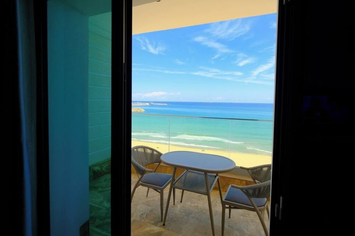 Un balcón con vista al océano, una mesa redonda y cuatro sillas.