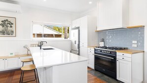 Una cocina moderna con armarios blancos, una isla central con taburetes, un horno empotrado y vistas al exterior a través de una ventana.