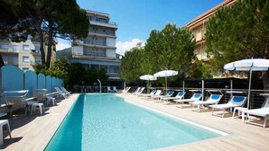 A rectangular swimming pool with lounge chairs and umbrellas, surrounded by trees and buildings. - Holiday apartment mit Klimaanlage und Pool (Pietra Ligure)