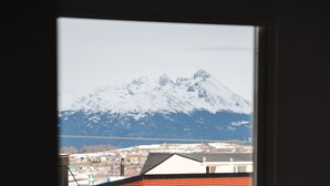 Una montaña con cima nevada, vista a través de una ventana con techo rojo y un edificio blanco al frente.
