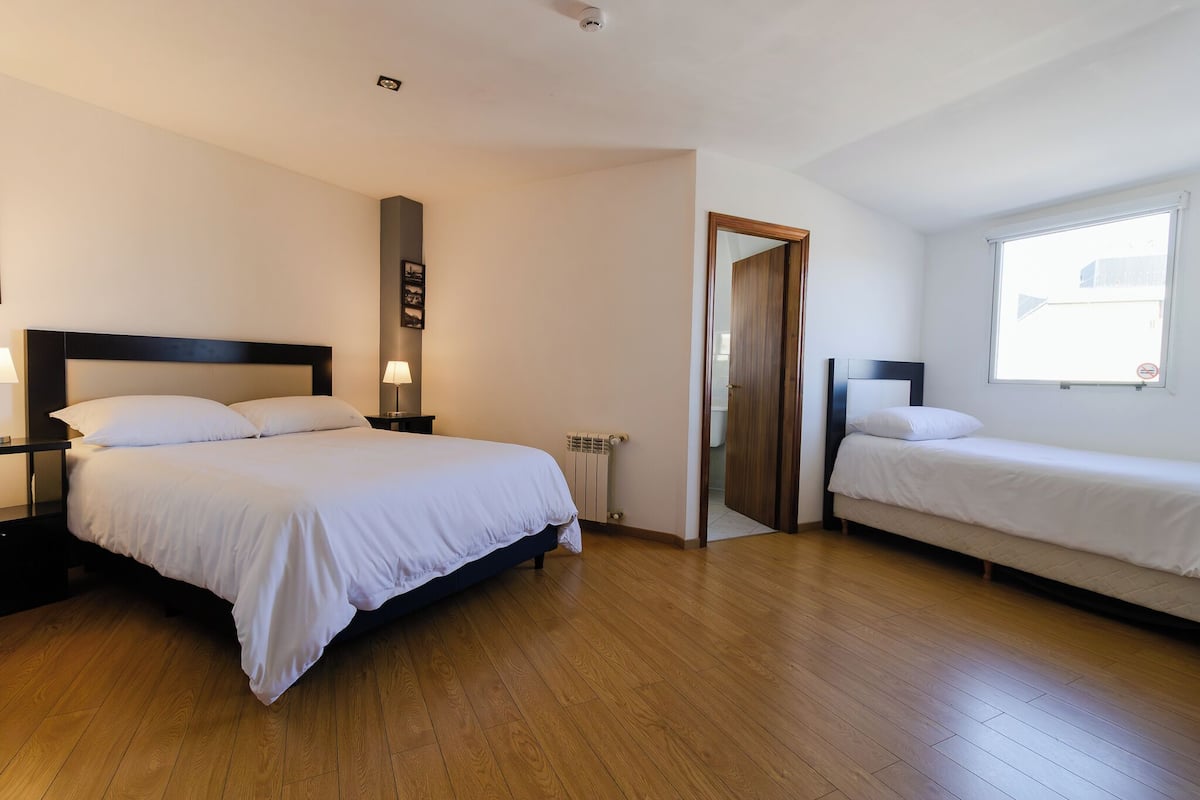 Habitación de hotel con una cama grande, una cama más pequeña, suelo de madera, un radiador y una ventana con vistas.