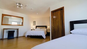 Habitación de hotel con una cama grande, una cama más pequeña, piso de madera, un espejo, una mesita de noche y una puerta.