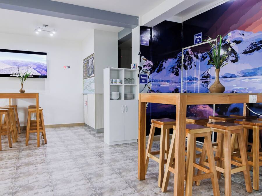 A hotel reception area with a wooden reception desk, a TV mounted on the wall, a white shelving unit, and a mural depicting a mountainous landscape.