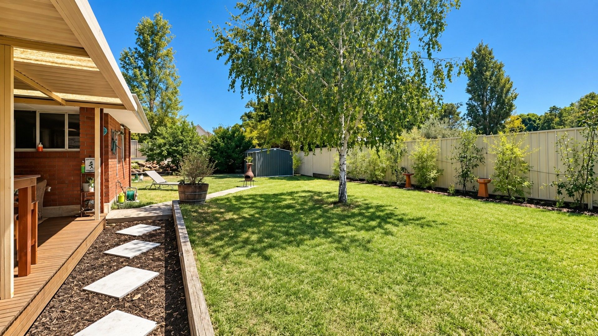 A backyard with a wooden deck, a lawn, a tree, and a shed.