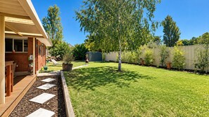 A backyard with a wooden deck, a lawn, a tree, and a shed.