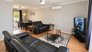 A modern living room with a black leather sofa, a wooden coffee table, and a television.