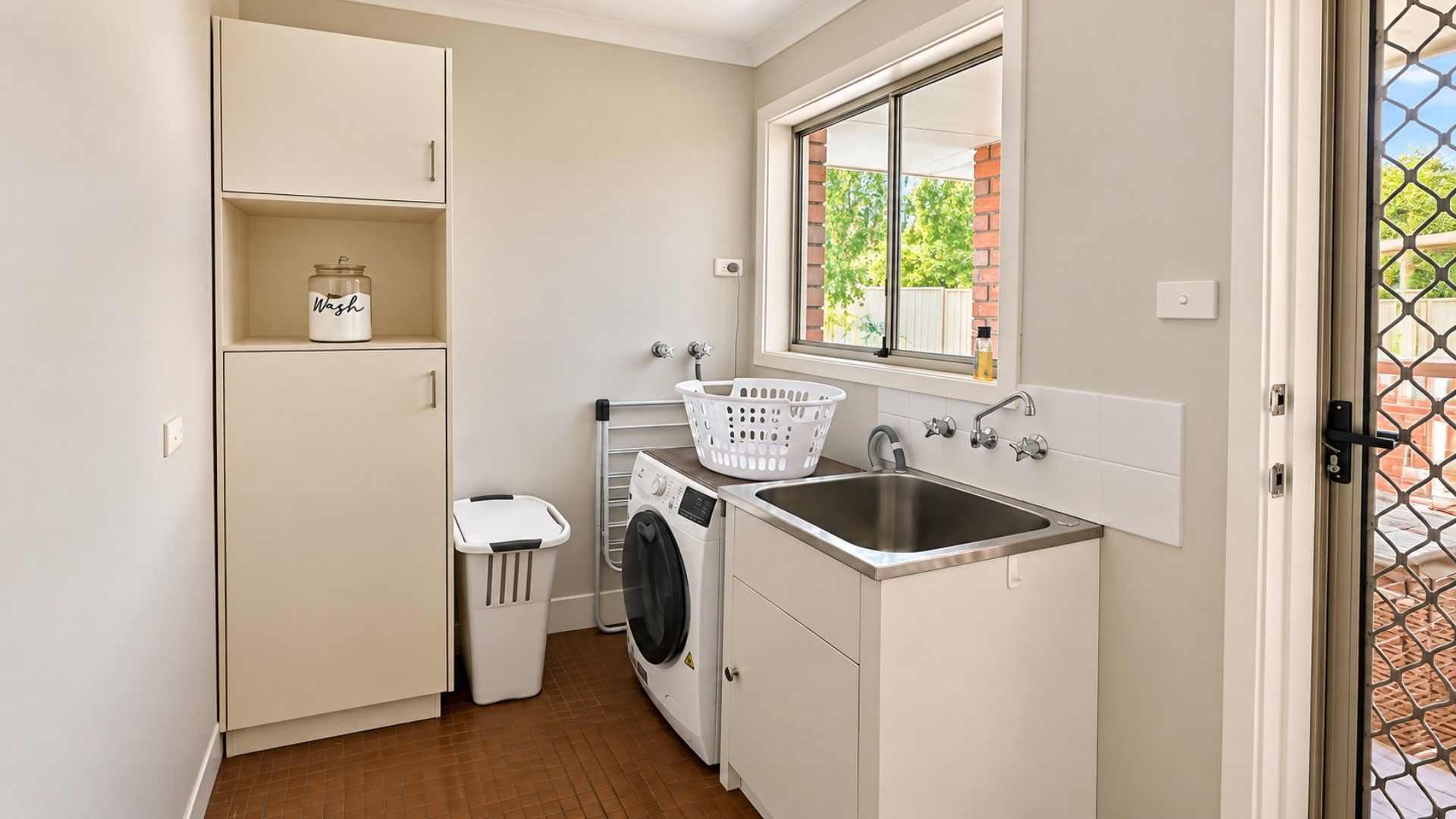 Une petite buanderie équipée d’un lave-linge, d’un évier, d’un étendoir et d’un panier à linge.