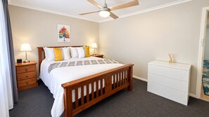 A bedroom with a wooden bed, two bedside tables with lamps, a ceiling fan, a white dresser, and a painting on the wall. - ### Central Nannup Holiday Home: Your Perfect Nature Retreat in the Heart of Nannup (Nannup)