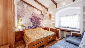 Een slaapkamer met een houten bed, een groot bloemenmuur, een raam met gordijnen en ingebouwde planken.