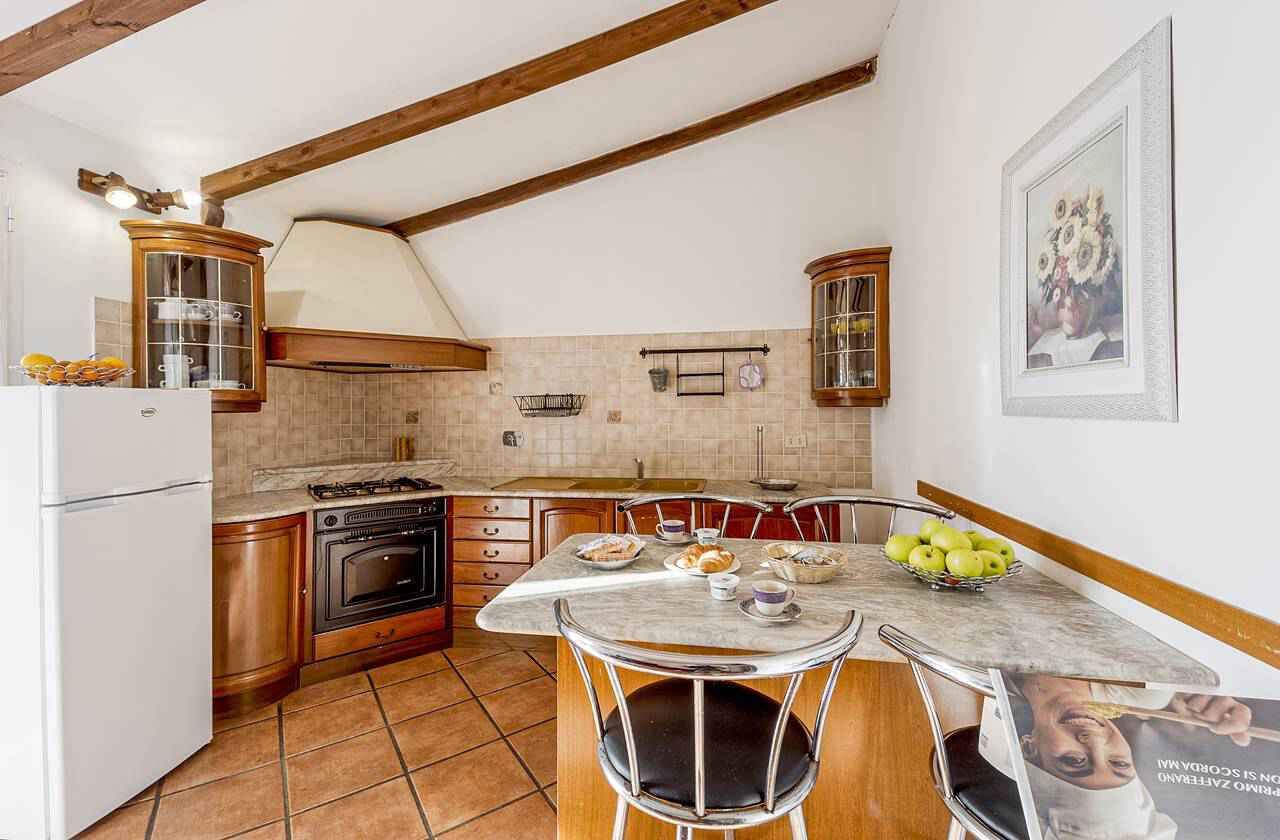 A kitchen with wooden cabinets, a stove, a refrigerator, and a dining table with chairs.