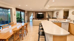 A modern kitchen with a central island, dining area with wooden chairs, and a sofa. - Anne's Retreat - Busselton (West Busselton)